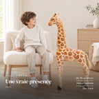 Peluche géante girafe avec un enfant dans une chambre lumineuse. Une vraie présence : 25, 70 ou 90 cm, pelage tacheté, dès 3 ans