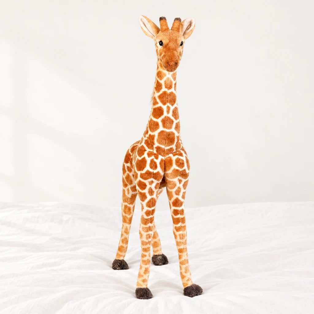 Peluche géante girafe posée sur un lit blanc, en pleine lumière