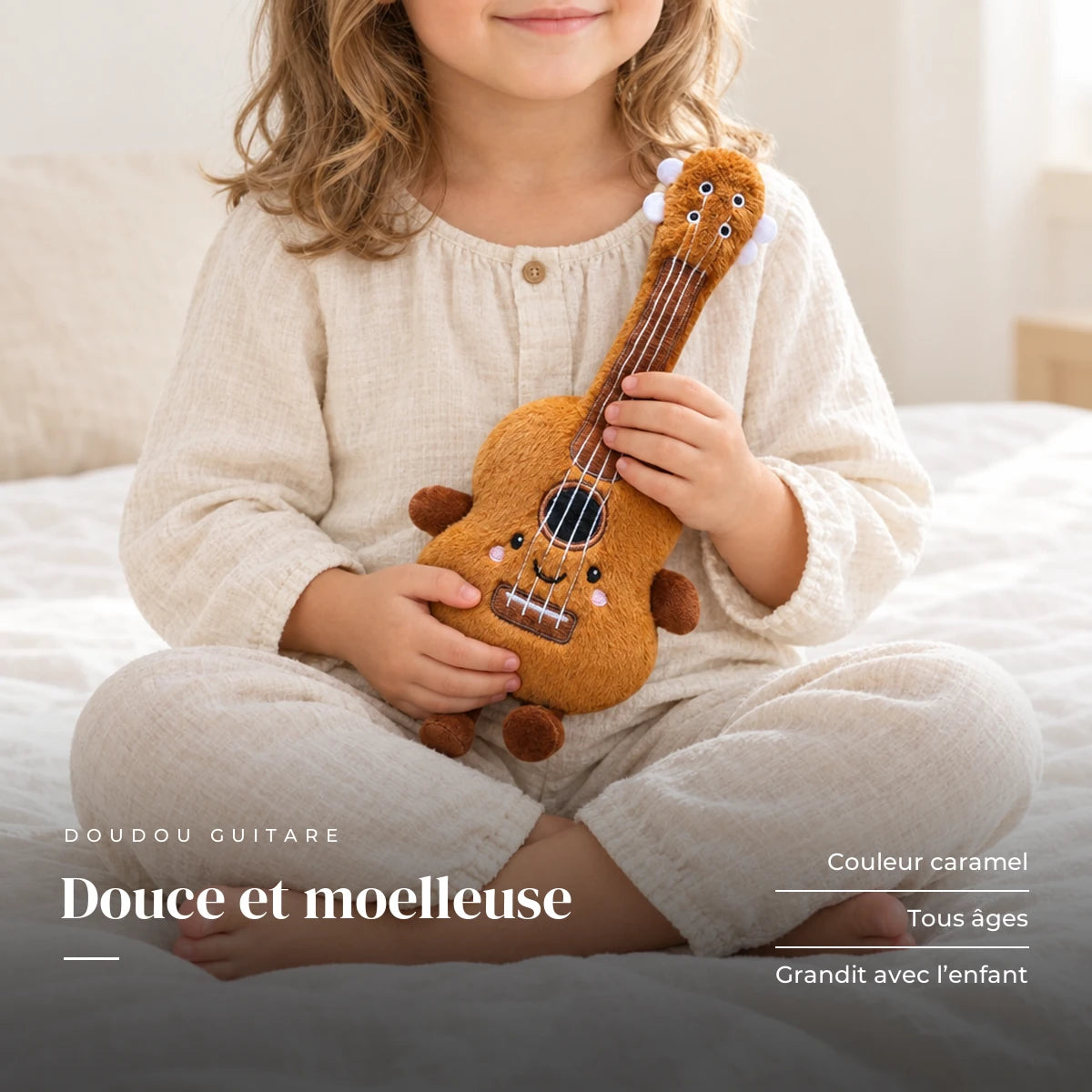 Peluche instrument kawaii guitare souriante tenue par un enfant pour montrer sa taille réelle. Douce et moelleuse : couleur caramel, tous âges, grandit avec l’enfant
