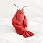 Peluche homard tout doux posée sur un lit blanc, en pleine lumière