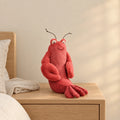 Peluche homard tout doux posée sur une table de chevet en bois clair
