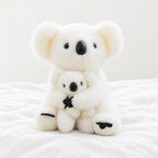Peluche koala avec son bébé blanche avec bébé posée sur un lit blanc, en pleine lumière