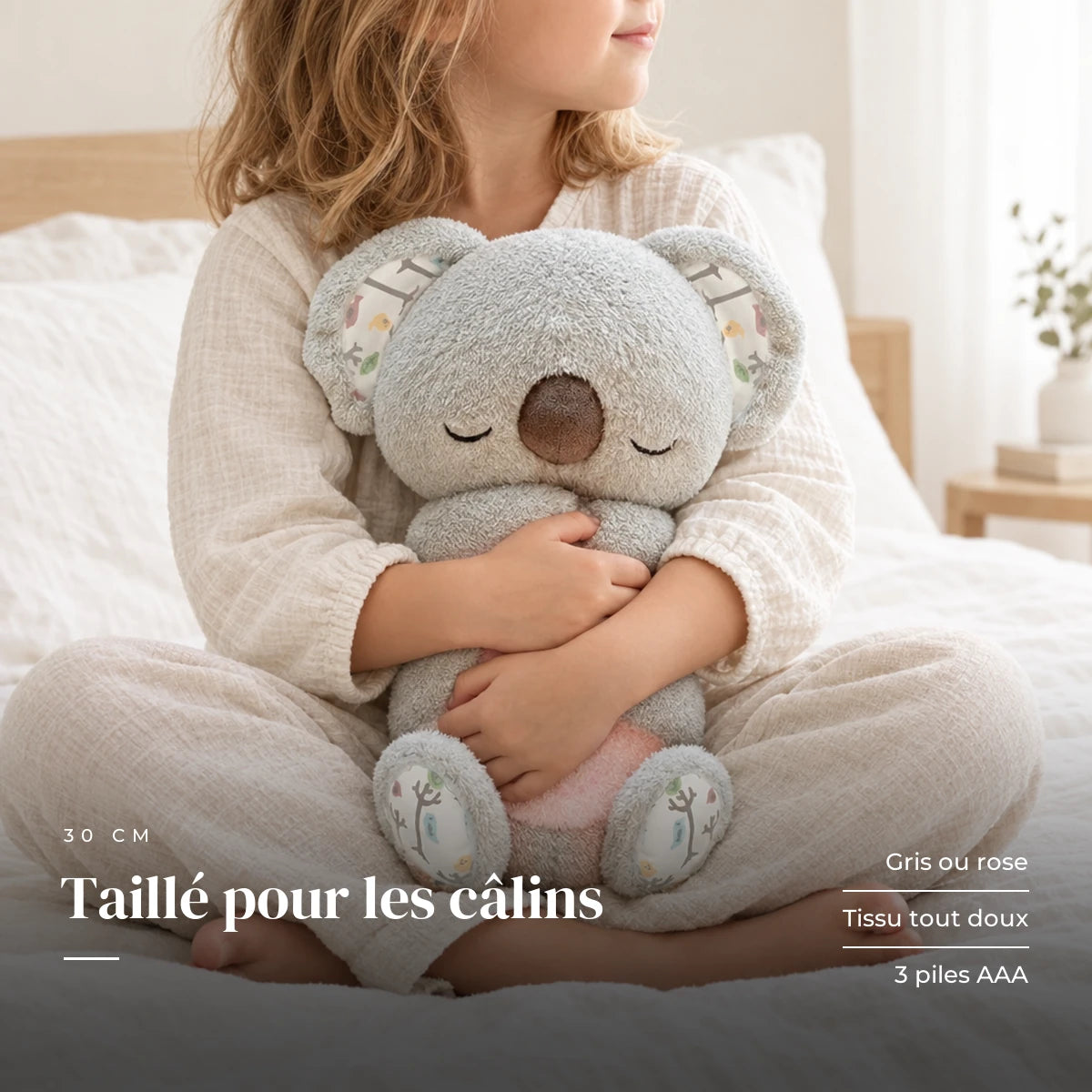 Peluche koala qui respire tenue par un enfant pour montrer sa taille réelle. Taillé pour les câlins : gris ou rose, tissu tout doux, 3 piles AAA