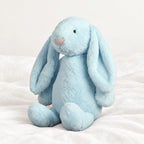 Lapin en peluche moelleux pour bébé bleu posé sur un lit blanc, en pleine lumière