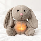 Peluche lapin qui respire posée sur un lit blanc, en pleine lumière