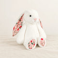 Lapin en peluche avec motif fleuri blanc sur fond crème, en studio