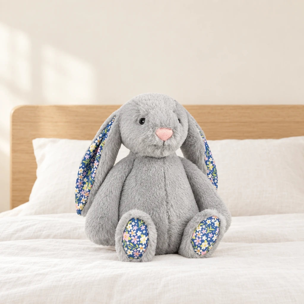 Lapin en peluche avec motif fleuri gris posé sur un lit en lin blanc