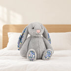 Lapin en peluche avec motif fleuri gris posé sur un lit en lin blanc