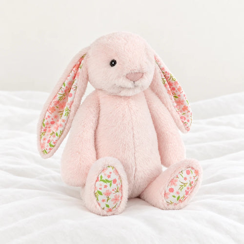 Lapin en peluche avec motif fleuri rose posé sur un lit blanc, en pleine lumière