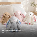 Lapin en peluche avec motif fleuri posé sur un lit en lin blanc. Le cadeau de naissance : motif fleuri, yeux brodés, dès la naissance