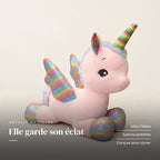 Peluche licorne féerique avec corne et ailes colorées posée sur un lit en lin blanc. Elle garde son éclat : ailes irisées, sabots pailletés, conçue pour durer