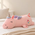 Peluche licorne rose veilleuse lumineuse et magique posée sur un lit en lin blanc