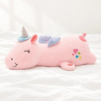 Peluche licorne rose veilleuse lumineuse et magique posée sur un lit blanc, en pleine lumière