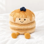 Peluche petit dej’ pancakes kawaii posée sur un lit blanc, en pleine lumière
