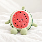 Peluche fruit kawaii pastèque gourmande posée sur un lit blanc, en pleine lumière