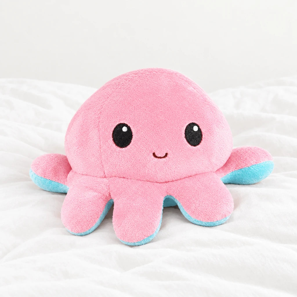 Peluche pieuvre réversible posée sur un lit blanc, en pleine lumière