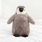 Peluche pingouin manchot câlin gris posée sur un lit blanc, en pleine lumière