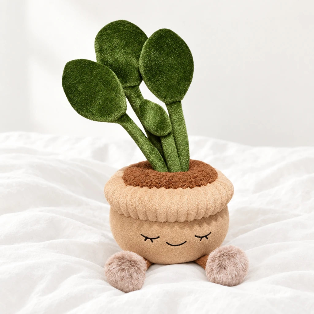 Peluche kawaii plante en pot rond posée sur un lit blanc, en pleine lumière