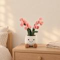 Peluche plante kawaii orchidée douce et colorée rose posée sur une table de chevet en bois clair