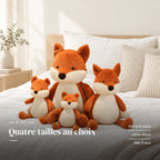 Peluche renard assis tout doux posée sur un lit en lin blanc. Quatre tailles au choix : renard assis, ultra-doux, dès 3 ans