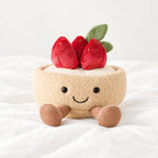 Peluche tarte fraise gourmande kawaii posée sur un lit blanc, en pleine lumière