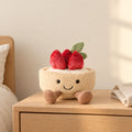 Peluche tarte fraise gourmande kawaii posée sur une table de chevet en bois clair