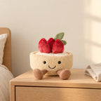 Peluche tarte fraise gourmande kawaii posée sur une table de chevet en bois clair