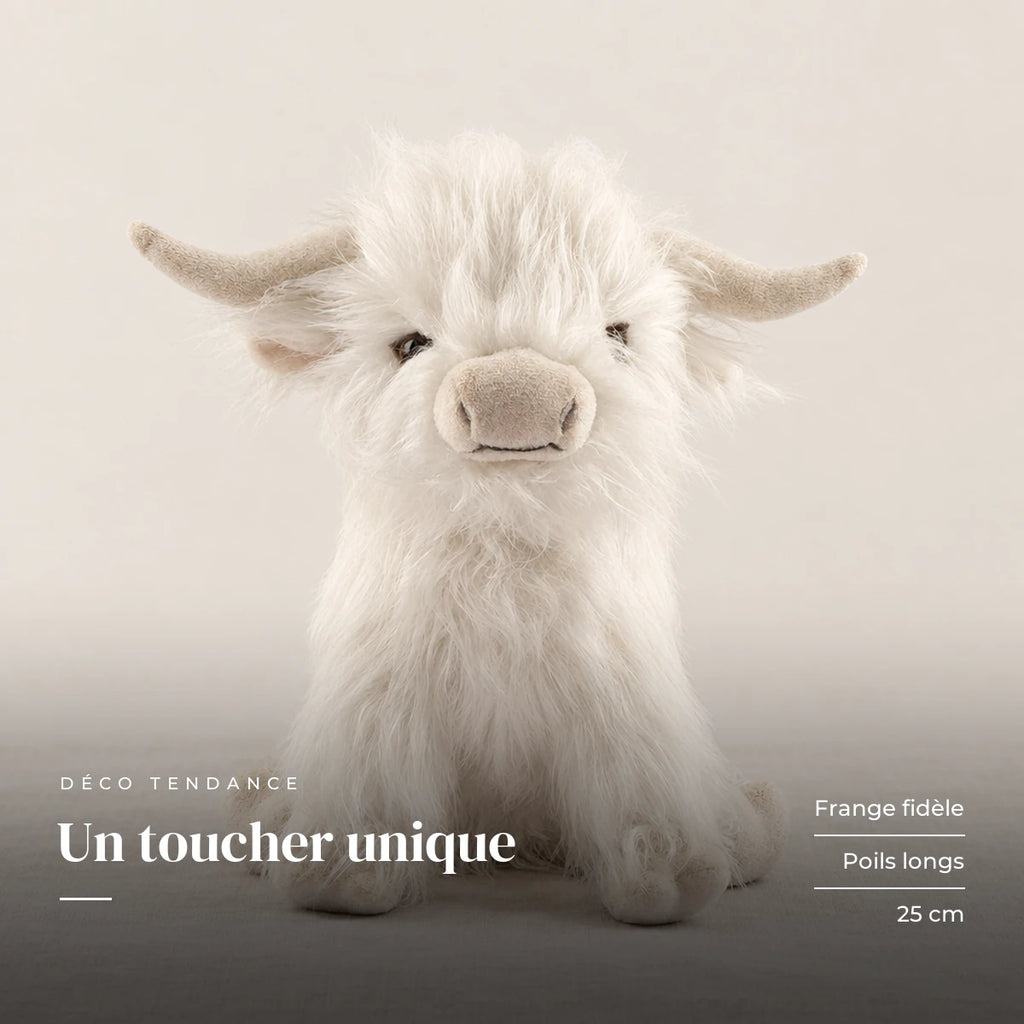 Peluche vache Highland à poils longs blanche sur fond crème, en studio. Un toucher unique : frange fidèle, poils longs, 25 cm