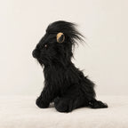 Peluche vache Highland à poils longs noire sur fond crème, en studio