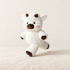 Peluche vache originale qui court blanche sur fond crème, en studio