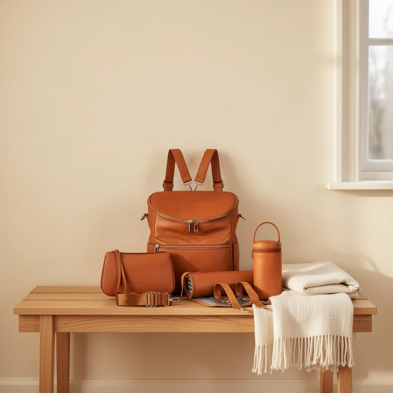 Sac à dos à langer simili cuir camel avec accessoires posé sur un banc dans une entrée