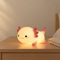 Veilleuse axolotl rechargeable en silicone allumée sur une table de chevet en chêne dans une chambre d’enfant