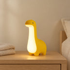 Veilleuse dinosaure bébé allumée sur une table de chevet en chêne dans une chambre d’enfant