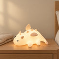 Veilleuse bébé dragon aimantée allumée sur une table de chevet en chêne dans une chambre d’enfant