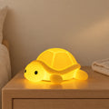 Veilleuse tortue bébé en silicone allumée sur une table de chevet en chêne dans une chambre d’enfant