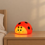 Veilleuse coccinelle rouge tactile allumée sur une table de chevet en chêne dans une chambre d’enfant