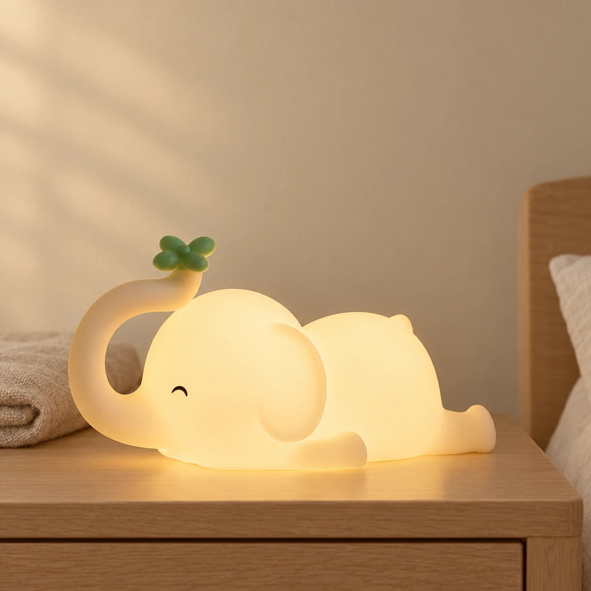 Veilleuse éléphant bébé tactile allumée sur une table de chevet en chêne dans une chambre d’enfant