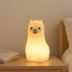 Veilleuse lama bébé rechargeable en silicone allumée sur une table de chevet en chêne dans une chambre d’enfant