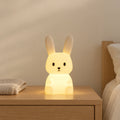 Veilleuse lapin enfant tactile allumée sur une table de chevet en chêne dans une chambre d’enfant