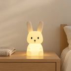 Veilleuse lapin enfant tactile allumée sur une table de chevet en chêne dans une chambre d’enfant