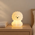 Veilleuse lion enfant avec télécommande allumée sur une table de chevet en chêne dans une chambre d’enfant