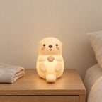 Veilleuse loutre en silicone rechargeable allumée sur une table de chevet en chêne dans une chambre d’enfant