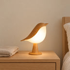 Veilleuse oiseau tactile avec diffuseur allumée sur une table de chevet en chêne dans une chambre d’enfant
