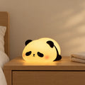 Veilleuse panda en silicone tactile et rechargeable allumée sur une table de chevet en chêne dans une chambre d’enfant