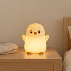 Veilleuse pingouin rechargeable allumée sur une table de chevet en chêne dans une chambre d’enfant