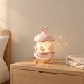Veilleuse projection bébé lapin musicale allumée sur une table de chevet en chêne dans une chambre d’enfant