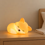 Veilleuse renard bébé rechargeable en silicone allumée sur une table de chevet en chêne dans une chambre d’enfant